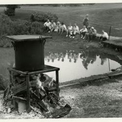 Fish Boil: kettle on flame, people seated by Meadow Lake in background
