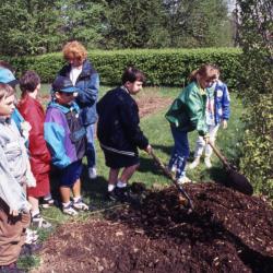 Group of children watch as boy and girl shovel soil at Arbor Day tree planting