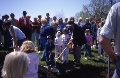 Adults and children planting tree with crowd watching on Arbor Day