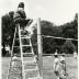 Deb Seymour, referee, seated on ladder looking over employee summer picnic volleyball game near the Research Building