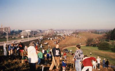 Groups of people scattered along berm, including Bill Hess with shovel in foreground, during Earth Day celebration and berm planting