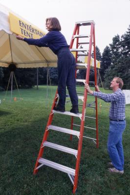 Linda Wetstein placing "Entertainment Tent" sign up for Family Fair, Rick Hootman holding ladder