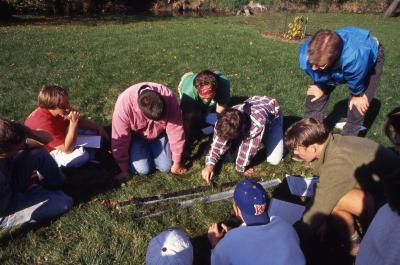 Pat Kelsey and students seated outside on ground looking at soil trench for Wheaton College soil class