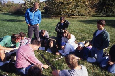 Pat Kelsey and students seated outside on ground measuring soil trench for Wheaton College soil class