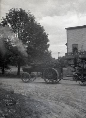 Man driving Lisle Farms threshing outfit in front of Riedy's drug store in Lisle