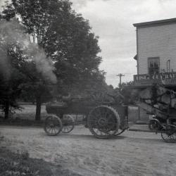 Man driving Lisle Farms threshing outfit in front of Riedy's drug store in Lisle