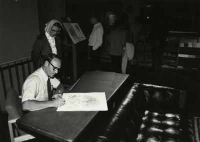 Tony Tyznik signing his artwork for woman at table 