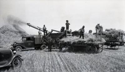 Group of men standing on top of threshing equipment at Lisle Farms