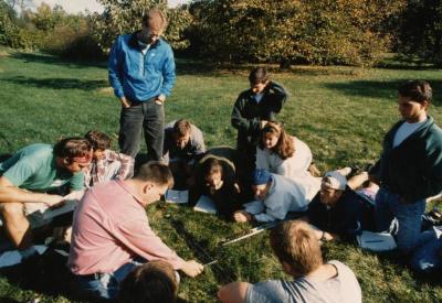 Pat Kelsey and class studying soil, seated on grass in an open field