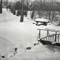 Snow-covered garden path in winter with wooden footbridge along Residence Drive, near Japanese Garden