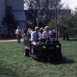 Dr. Tom Green and Karla Patterson in cart leading line of people across lawn near Research building for tree planting at Arborfest