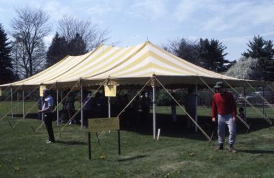 Yellow striped tent with visitors inside and around next to Arborfest sign for tickets and information