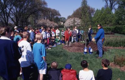 Deb Seymour speaking to crowd, mainly children, at Arbor Day tree planting near Hedge Garden