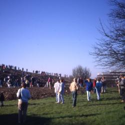 Crowd on and walking toward berm with building at right in distance on Earth Day