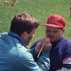 Kris Bachtell face painting mustache on young boy during Arbor Week