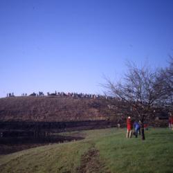 View from alongside Crabapple Lake toward berm with crowd lined up on top of berm on Earth Day