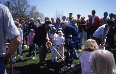 Crowd with two adults, one with hat, and three children planting tree on Arbor Day
