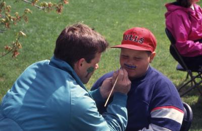 Kris Bachtell face painting mustache on young boy during Arbor Week