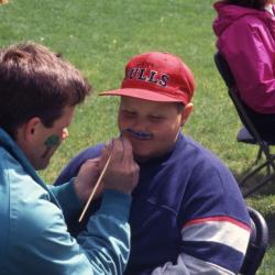 Kris Bachtell painting mustache on boy during Arbor week