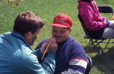 Kris Bachtell painting mustache on boy during Arbor week