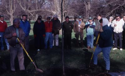 George Ware and other employee shovel soil over newly planted tree at Arbor Day employee tree planting