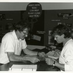 Doris Taylor examining plant leaves with man at Plant Clinic desk