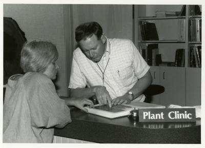 Ed Hedborn reviewing images of plants in book with woman at Plant Clinic desk