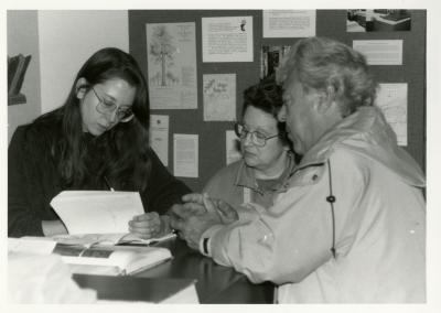 Rose Rieger reviewing plant books with woman and man at Plant Clinic desk