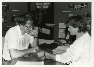 Doris Taylor examining plant leaves with man at Plant Clinic desk