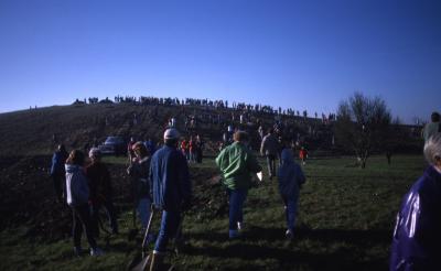 Crowd walking toward berm with shovels during Earth Day celebration and berm planting