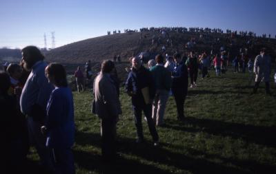 Dr. Marion Hall holding folder standing with crowd below berm during Earth Day celebration and berm planting