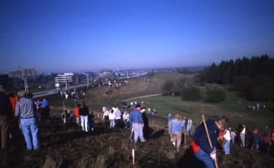 View along top and length of berm of crowd planting trees during Earth Day celebration and berm planting