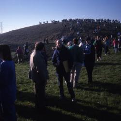 Dr. Marion Hall holding folder standing with crowd below berm during Earth Day celebration and berm planting