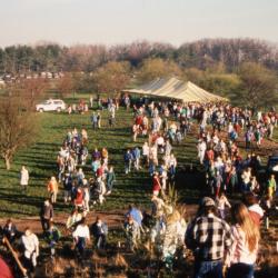 View from top of berm of crowd and yellow stripe tent during Earth Day celebration and berm planting
