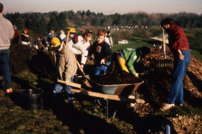 Children loading wheelbarrow with mulch during Earth Day celebration and berm planting