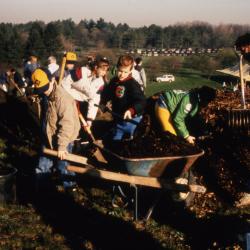 Children loading wheelbarrow with mulch during Earth Day celebration and berm planting