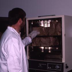 Pat Kelsey in lab coat shifting material in Constant Temperature Oven in lab