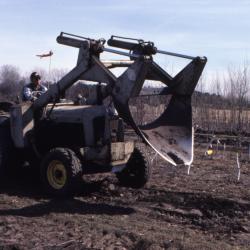 Grounds staff person driving tractor with blade attached to the front, used for transplanting trees