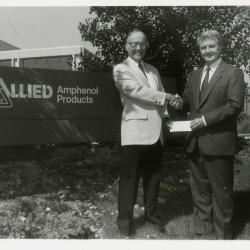 Dr. Marion Hall receiving check and shaking hands with man in front of Allied Amphenol Products
