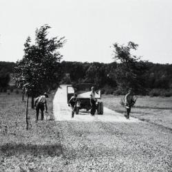 Workers covering freshly sprayed asphalt roadbed with gravel