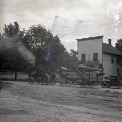 Lisle Farms threshing outfit and automobile in front of Riedy's Drug Store in Lisle, angled view