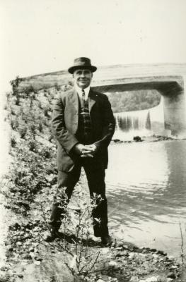 John Van Gemert standing at edge of water in front of bridge and dam