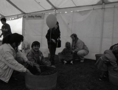 Arbor Day activities at The Morton Arboretum, boy playing with woman in barrel of dirt next to Seedling Planting station