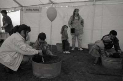 Arbor Day activities at The Morton Arboretum, boy planting plant with woman in barrel of dirt next to Seedling Planting station