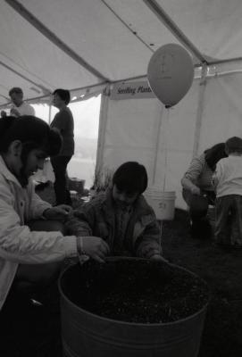 Arbor Day activities at The Morton Arboretum, boy working with woman in barrel of dirt next to Seedling Planting station