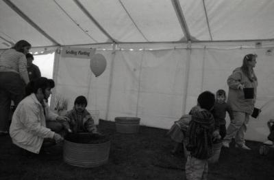 Arbor Day activities at The Morton Arboretum, boy scooping dirt with woman in barrel next to Seedling Planting station