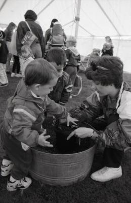 Arbor Day activities at The Morton Arboretum, woman and two boys transferring plant to dirt in barrel next to Seedling Planting station