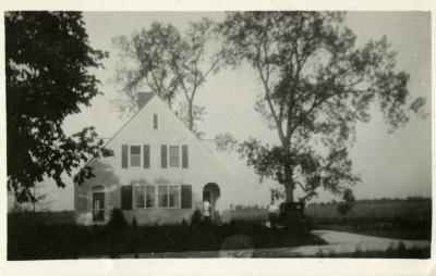 Clarence Godshalk's first Arboretum house, front exterior view, Harriet standing in doorway, Clarence at car