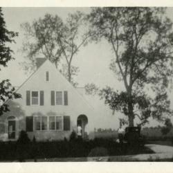 Clarence Godshalk's first Arboretum house, front exterior view, Harriet standing in doorway, Clarence at car